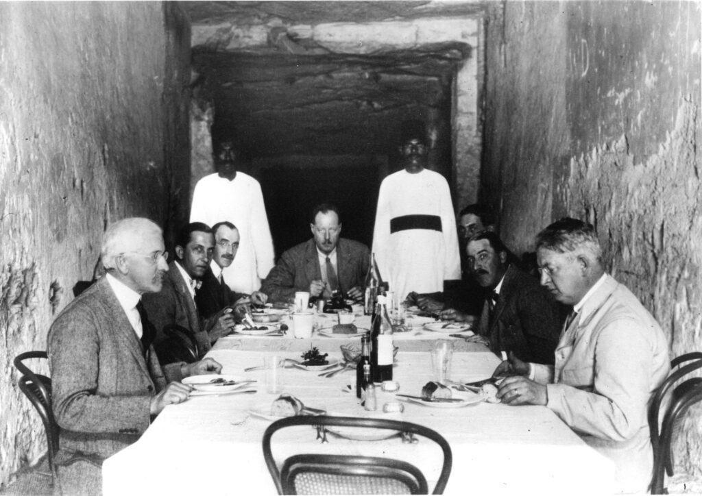 Allan Gardiner, geheel rechts, zit naast Howard Carter tijdens een lunch in het voorjaar van 1923 in het nooit in gebruik genomen graf van Ramses XI